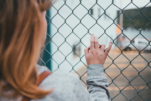Photo: a person is seen touching a chain link fence, facing away from the camera 