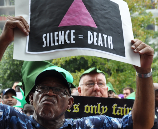 Photo of a protester holding up a sign with a pink triangle against a black background, beneath the triangle in white, 