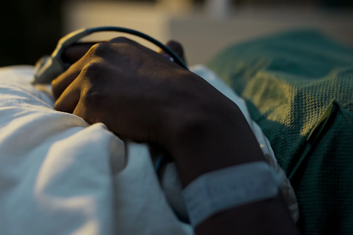 Photo of a close-up of a person in a hospital bed, hands folded their blanket