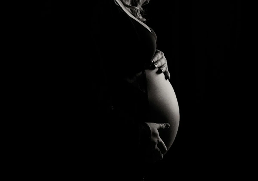 Photo of a pregnant belly in dark dramatic lighting.