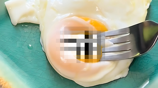 Photo of a sunny-side-up egg yolk being punctured by a fork, the leaky yolk pixilated