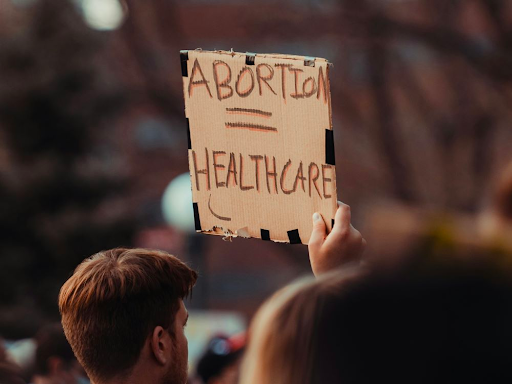 A man holds a handwritten sign up that reads Abortion = Healthcare
