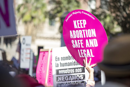 Photo: protesters holding up signs, one of which is pink, round, and says 