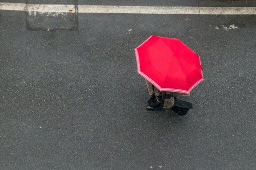 Photo of a bird's eye view of a person walking on a paved street, holding an open red umbrella.
